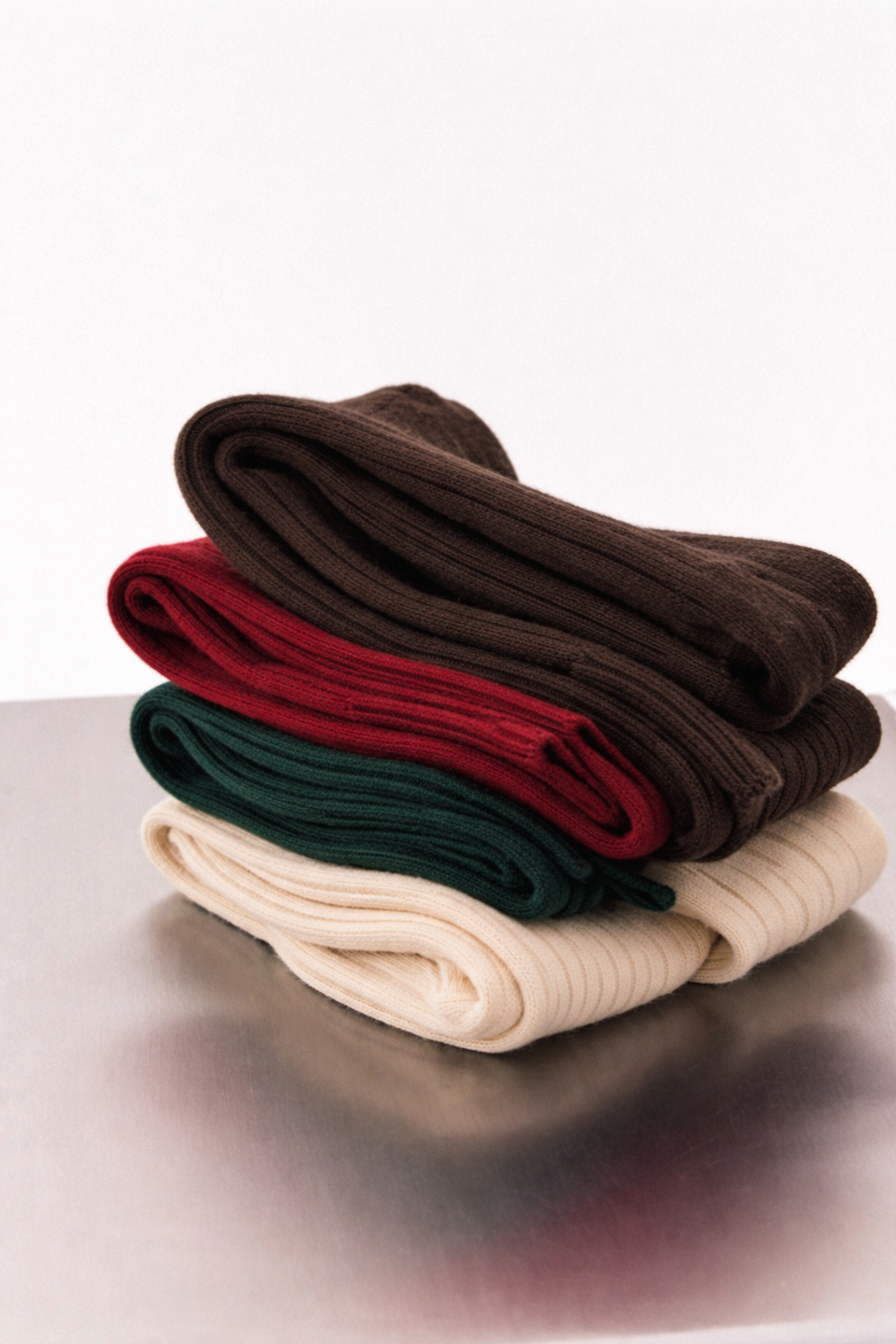 Stack of folded socks in brown, red, green, and beige on a reflective surface.
